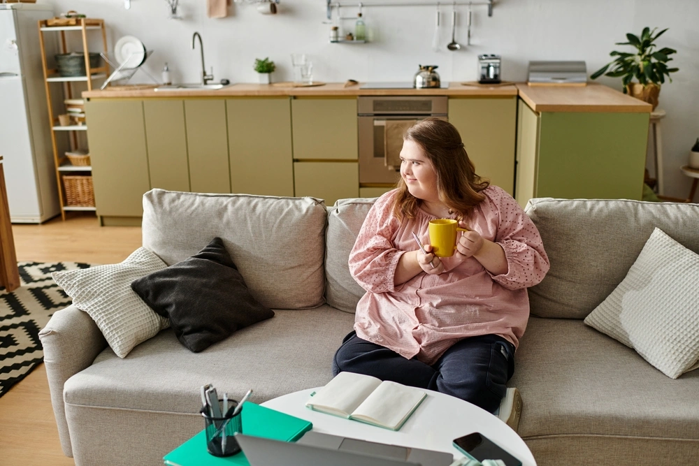 disabled women with down syndrome disability sitting on sofa in her home and drinking coffee